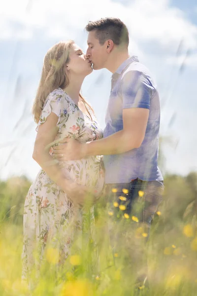 Jong gelukkig zwanger paar in liefde hand in hand, ontspannen in weide. — Stockfoto