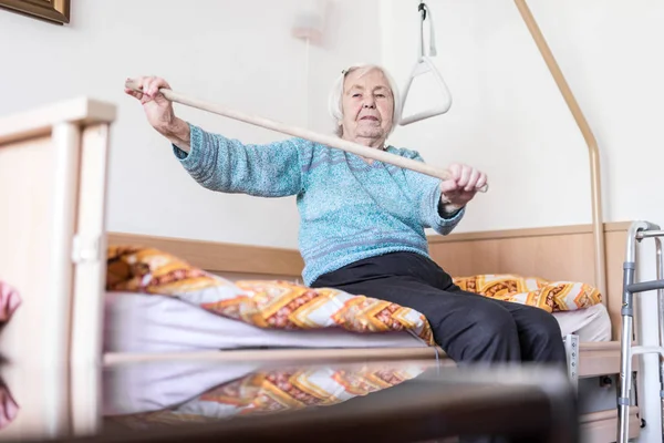 Idoso 96 anos de idade mulher se exercitando com um pau sentado em seu mau. — Fotografia de Stock