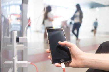 Elektrikli fiş ve şarj kablosu kullanarak halka açık bir yerde şarj ederken akıllı telefonu tutan ve kullanan kadın elleri