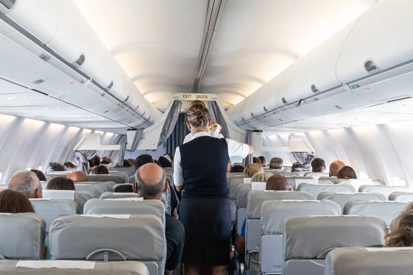 Interiör i kommersiella flygplan med flygvärdinna som betjänar passagerare på sittplatser under flygning. — Stockfoto