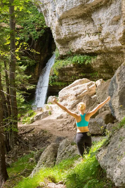 Active woman raising arms inhaling fresh air, feeling relaxed in nature.