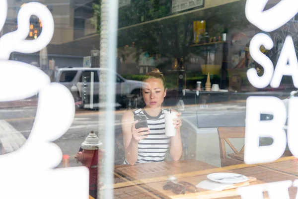 Thoughtful woman reading news on mobile phone during rest in coffee shop. — Stock Photo, Image