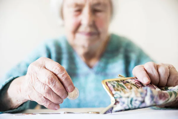 Besorgte ältere Frau sitzt am Tisch und zählt Geld im Portemonnaie. — Stockfoto