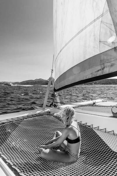 Beautiful woman relaxing on a summer sailing cruise, sitting and sunbathing in hammock of luxury catamaran sailing around Maddalena Archipelago, Sardinia, Italy. — Stock Photo, Image