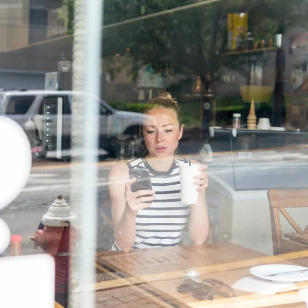 Kahve dükkanında dinlenirken cep telefonuyla haber okuyan düşünceli bir kadın.. — Stok fotoğraf