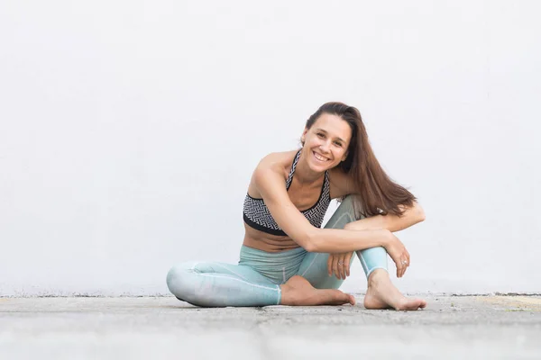 Fit sporty active girl in fashion sportswear sitting on the floor in front of gray wall.