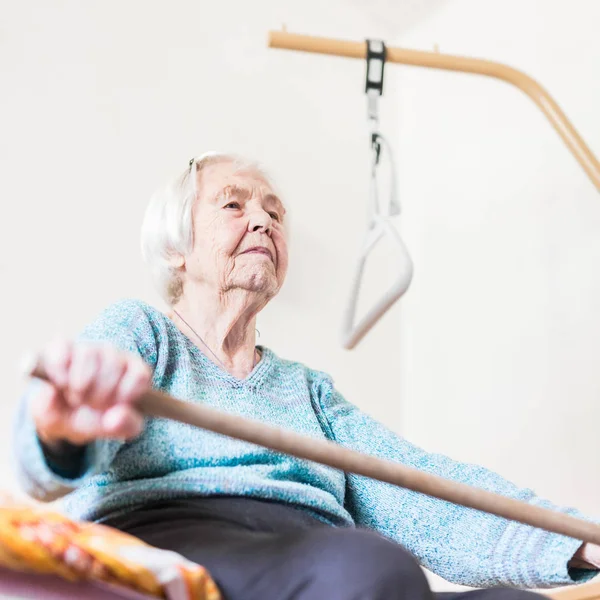 Ältere 96-jährige Frau übt mit einem Stock auf ihrem Bad sitzend. — Stockfoto