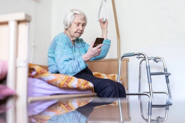 Starší 96 let čte stařena, když sedí na lékařské posteli a podpoří ji držitelem. — Stock fotografie