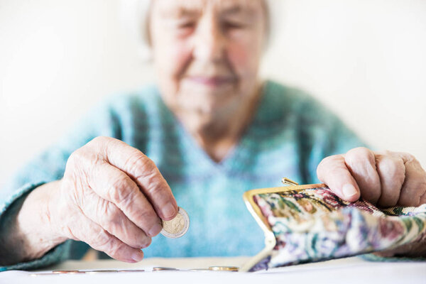 Concerned elderly woman sitting at the table counting money in her wallet.