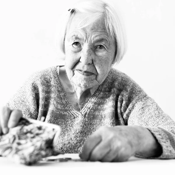 Eine besorgte ältere Frau sitzt am Tisch und zählt Geld in ihrem Portemonnaie. Schwarz-Weiß-Foto. — Stockfoto