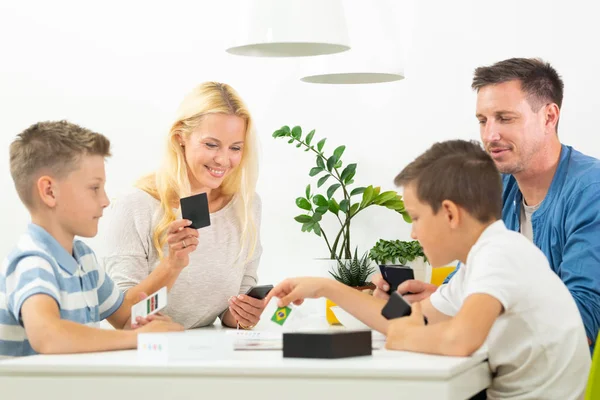 Happy young family playing card game at dining table at bright modern home.