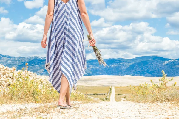 Detail einer Frau im Sommerkleid, die einen Strauß Lavendelblüten in der Hand hält, während sie im Sommer auf der Insel Pag im Freien durch trockene felsige mediterrane Küstenlandschaft spaziert — Stockfoto