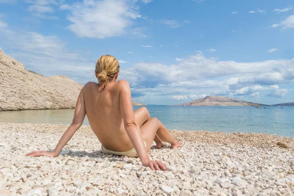 Vue arrière de la jeune femme caucasienne sexy bronzer seins nus sur la plage de pabble romote sur l'île de Pag, Croatie, Méditerranée . — Photo