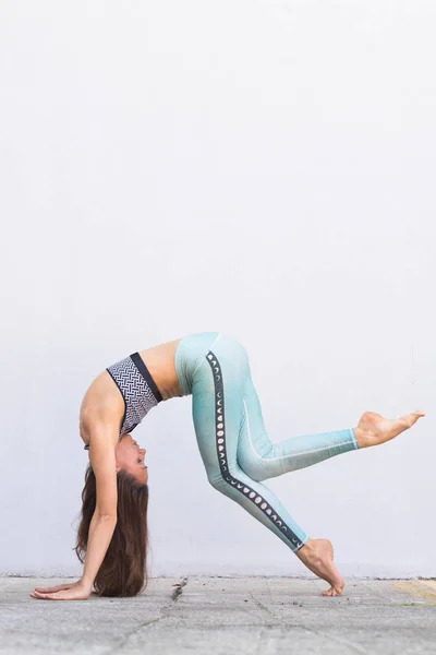 Chica activa deportiva en ropa deportiva de moda haciendo ejercicio de yoga fitness frente a la pared gris, deportes al aire libre, estilo urbano —  Fotos de Stock