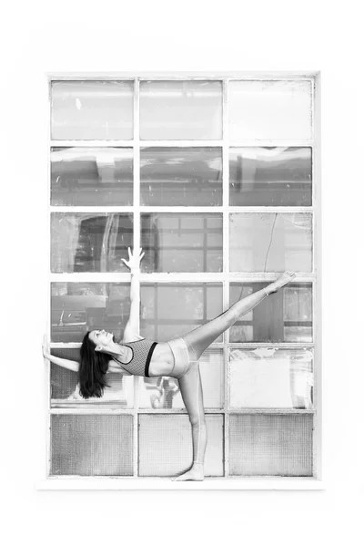 Ajuste deportivo chica activa en ropa deportiva de moda haciendo ejercicio de yoga fitness frente a un gran marco de ventana industrial. reflejos coloridos en vidrio de ventana. Yoga de estilo urbano. Blanco y negro —  Fotos de Stock