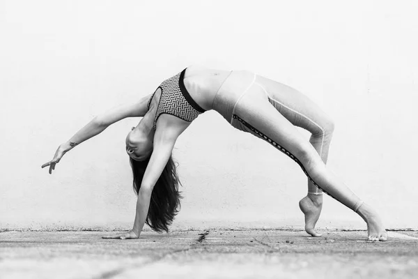 Fit sportig aktiv tjej i mode sportkläder gör yoga Fitness övning framför grå vägg, utomhussporter, urban stil. Svartvitt foto. — Stockfoto