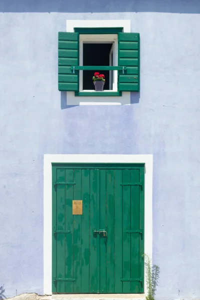Linda casa retro púrpura con ventana de madera verde con persianas y flores en la olla y puerta verde con marco blanco . —  Fotos de Stock