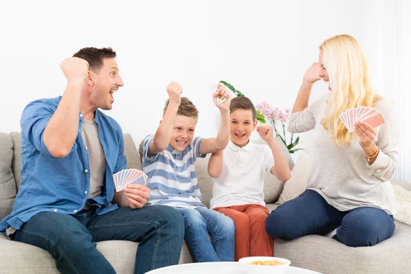 Feliz familia jugando al juego de cartas en el sofá de la sala de estar en casa y divertirse juntos celebrando el ganador del juego —  Fotos de Stock