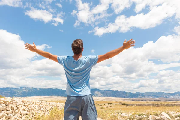 Vista trasera de hombre deportivo casual de pie en un camino de tierra país levantando las manos hasta las nubes en un cielo azul de verano. Concepto libertad y aventura de viaje . —  Fotos de Stock