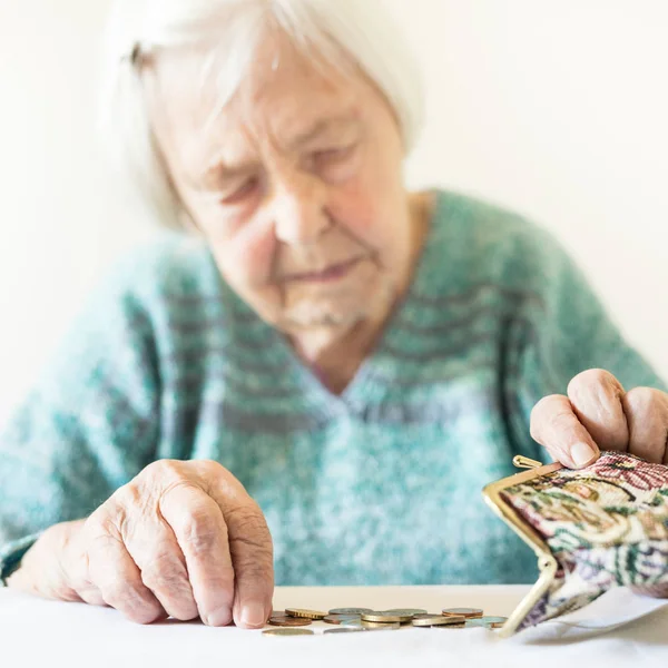 Besorgte ältere Frau sitzt am Tisch und zählt Geld im Portemonnaie. — Stockfoto