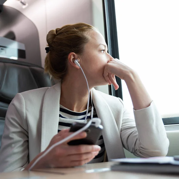 Pensativa mujer de negocios escuchando podcast en el teléfono móvil mientras viaja en tren. — Foto de Stock