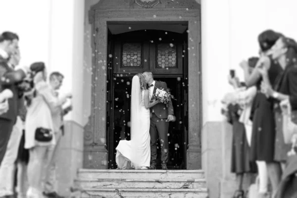 Молодята цілуються під час виходу з церкви після весільної церемонії, сім'я та друзі святкують свою любов з душем мильних бульбашок, звичаєм підірвати традиційну рисову ванну — стокове фото