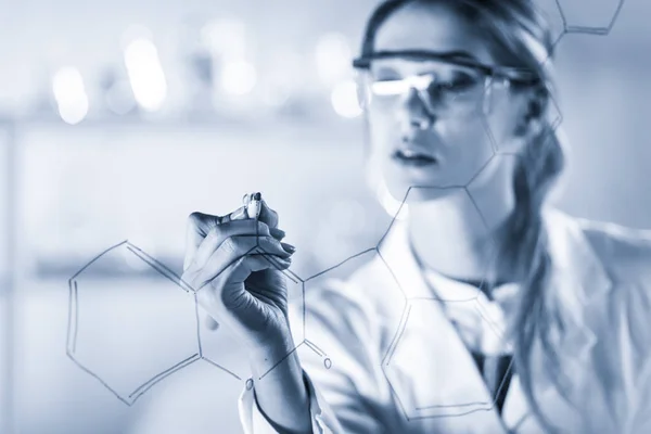 生命科学实验室一位自信的女研究员在玻璃板上书写结构化学公式的画像. — 图库照片