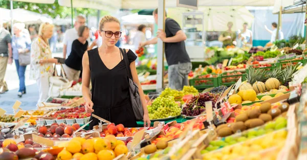 Kadın yerel gıda pazarından meyve ve sebze alıyor. Çeşitli organik sebzelerle market tezgahı — Stok fotoğraf