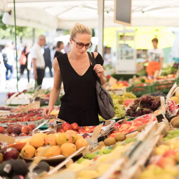 Woman buying fruits and vegetables at local food market. Market stall with variety of organic vegetable