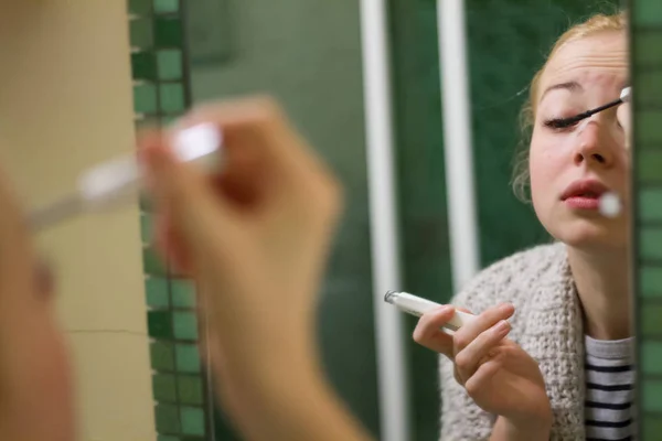 Morning routine. Casual beautyful woman applying maskara makeup in front of a mirror in the morning