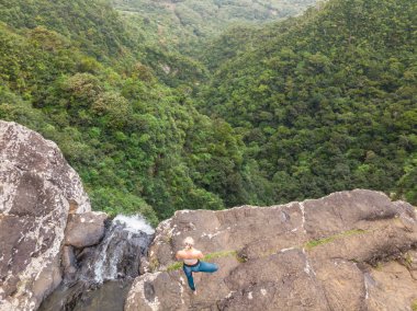 Aktif sportif kadın doğada rahatlatıcı, Mauritius tropik cennet adasında Black river gorges milli parkta 500 metre şelale tarafından yüksek clif yoga