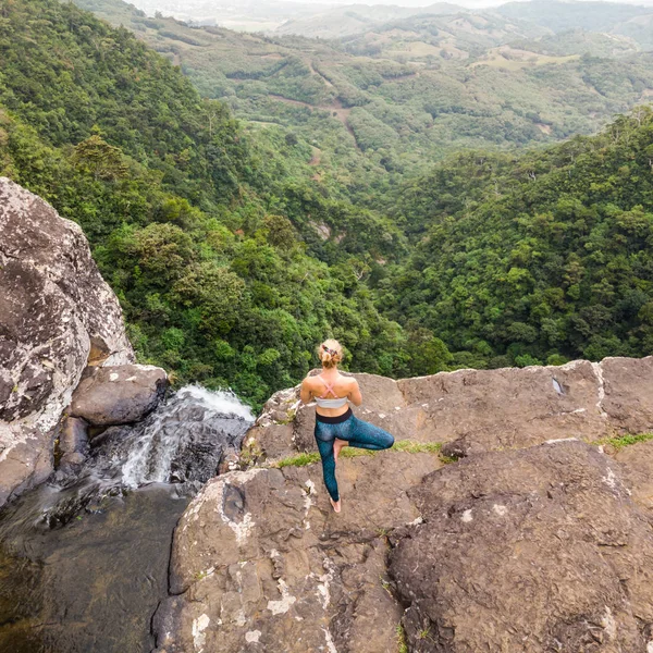 Active sporty woman relaxing in nature, practicing yoga on high clif by 500 feet waterfall at Black river gorges national park on tropical paradise island of Mauritius — Stock Photo, Image
