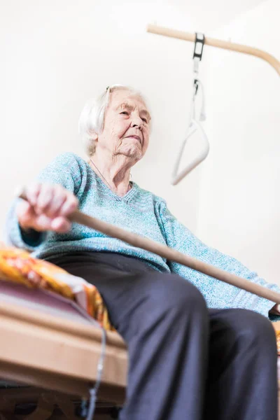 Elderly 96 years old woman exercising with a stick sitting on her bad. Stock Picture