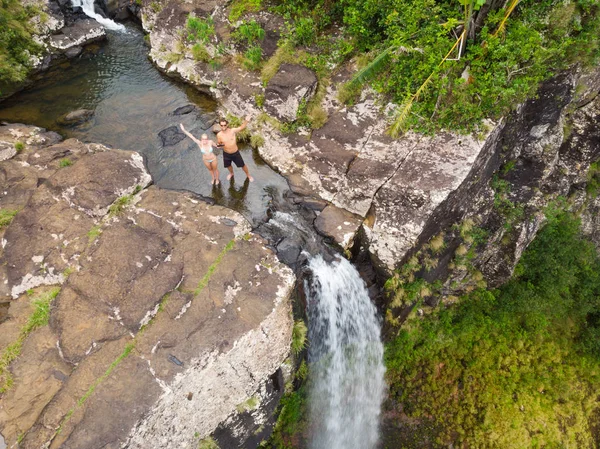 Εναέρια κορυφή θέα του ταξιδιωτικού ζευγαριού που χαιρετά το τηλεκατευθυνόμενο, στέκεται στην άκρη του καταρράκτη 500 ποδιών στη ζούγκλα του τροπικού νησιού του μαύρου ποταμού στο νησί του Μαυρικίου — Φωτογραφία Αρχείου