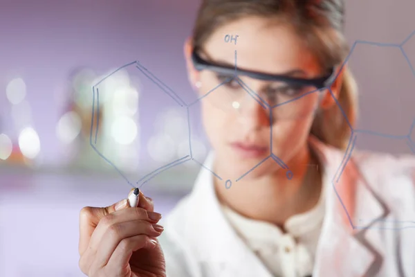 Portrait of a confident female researcher in life science laboratory writing structural chemical formula on a glass board. Royalty Free Stock Images