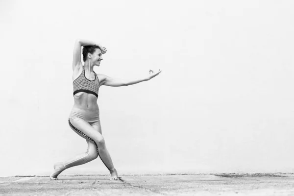 Ajuste deportivo chica activa en ropa deportiva de moda haciendo ejercicio de yoga fitness frente a la pared gris, deportes al aire libre, estilo urbano. Foto en blanco y negro . —  Fotos de Stock