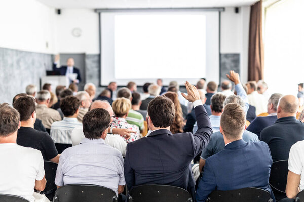 У меня к вам вопрос. Группа деловых людей сидит в конференц-зале. Бизнесмен поднимает руку. Конференция и презентация. Бизнес и предпринимательство