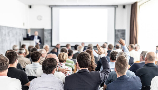 У меня к вам вопрос. Группа деловых людей сидит в конференц-зале. Бизнесмен поднимает руку. Конференция и презентация. Бизнес и предпринимательство
