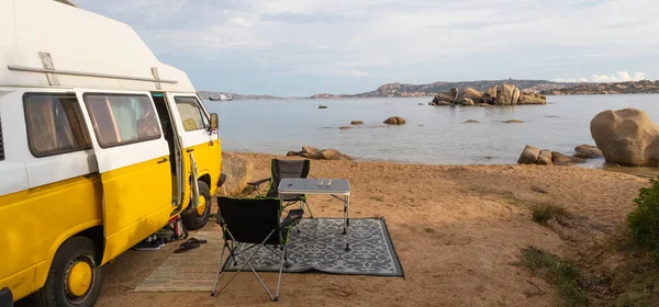 Old colorful retro camper van on camping site at beautiful rocky coastal landscape of Costa Smeralda, north east Sardinia, Italy. Tourism vacation and travel.