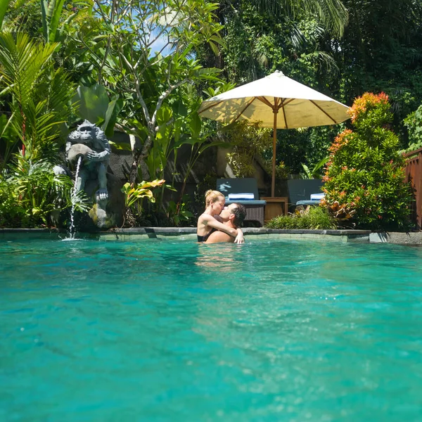 Feliz pareja besándose mientras se relaja en la piscina infinita spa al aire libre rodeado de exuberante vegetación tropical de Ubud, Bali. Spa de lujo y concepto de retiro de vacaciones de bienestar —  Fotos de Stock