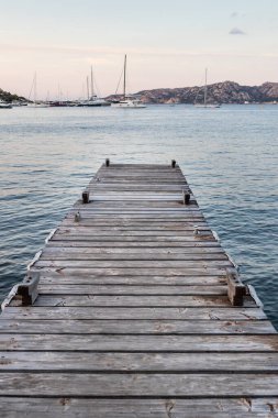 Ahşap iskele ve arka planda demirleyen yelkenliler muhteşem Porto Rafael denizi, Costa Smeralda, Sardinya, İtalya. Rahatlama, zenginlik, boş zaman aktivitesi sembolü