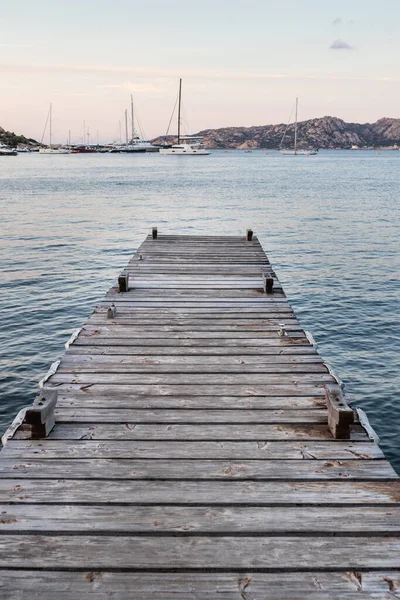 Muelle de madera y veleros amarre en el fondo al atardecer tranquilo mar de maravilloso Porto Rafael, Costa Esmeralda, Cerdeña, Italia. Símbolo para la relajación, la riqueza, la actividad de ocio — Foto de Stock