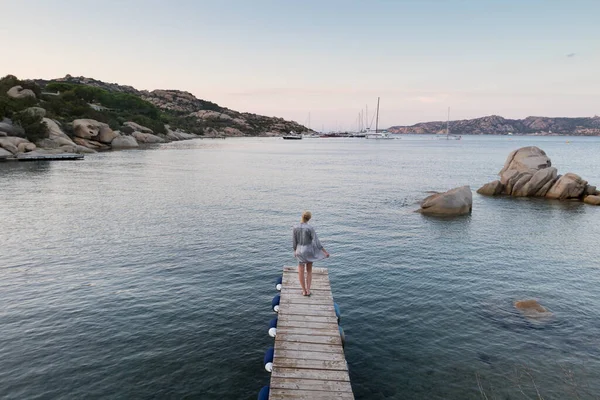 Hermosa mujer en vestido de verano de lujo de pie en el muelle de madera disfrutando de un paisaje marino tranquilo al atardecer. Vacaciones, resort y viajes . —  Fotos de Stock