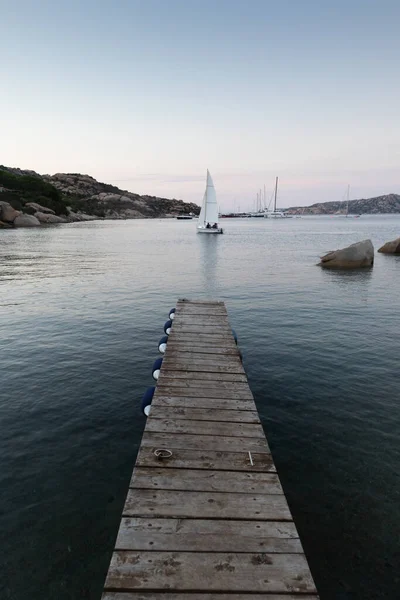 Muelle de madera y veleros navegando en el tranquilo mar de noche del maravilloso Porto Rafael, Costa Esmeralda, Cerdeña, Italia. Símbolo para la relajación, la riqueza, la actividad de ocio — Foto de Stock