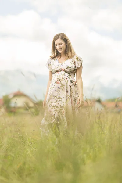 Mulher grávida bonita em vestido de verão branco no prado cheio de flores amarelas florescendo . — Fotografia de Stock