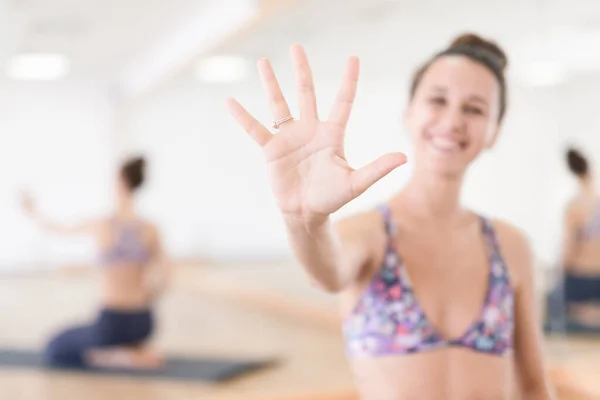 Fit sportlich aktive Frau lächelnd, in modischer Sportbekleidung, die eine offene Handfläche in die Kamera im Yoga-Studio zeigt. Aktiver urbaner Lebensstil. — Stockfoto