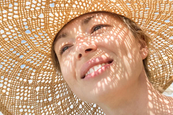 Retrato de cerca de una mujer con sombrero de paja disfrutando del sol de verano. Patrón de sombras cayendo sobre su rostro —  Fotos de Stock