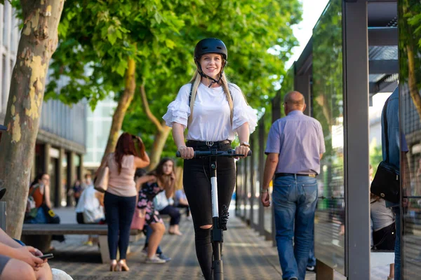 Adolescente fashinable de moda, hermosa chica rubia montando scooter eléctrico de alquiler público en el entorno urbano de la ciudad. Transporte urbano público moderno respetuoso del medio ambiente —  Fotos de Stock