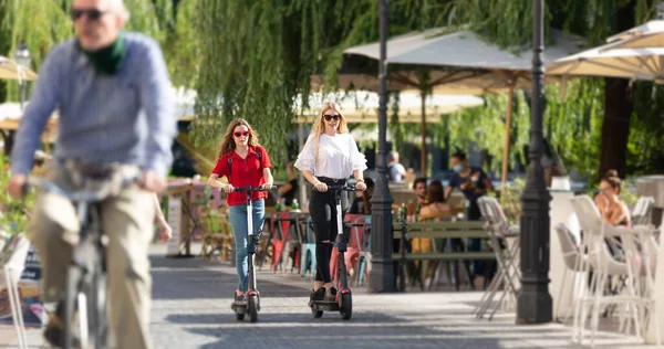 Trendiga fashinable tonårstjejer rider offentliga uthyrning elektriska skotrar i stadsmiljö. Ny miljövänlig modern kollektivtrafik i Ljubljana, Slovenien — Stockfoto