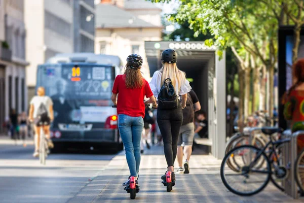 Bakifrån av trendiga fashinable tonårstjejer rida offentliga uthyrning elektriska skotrar i stadsmiljö. Ny miljövänlig modern kollektivtrafik i Ljubljana, Slovenien — Stockfoto